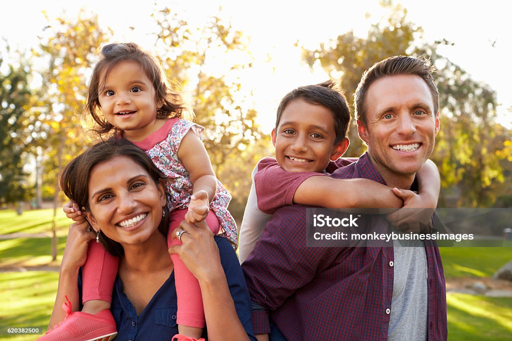 Mixed race parents carry their kids piggyback in a park